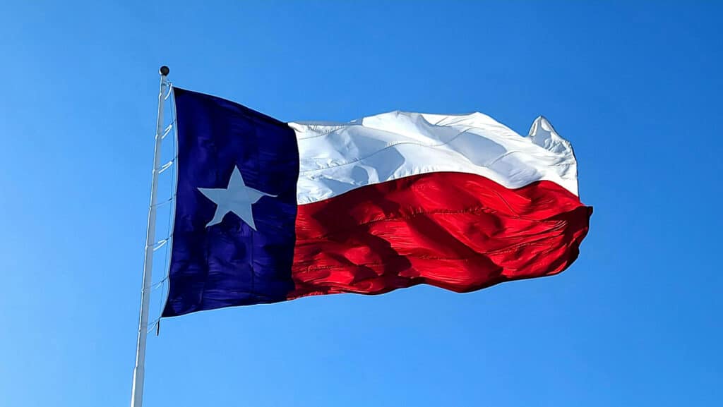 The flag of Texas is raised high in the wind on a clear day.