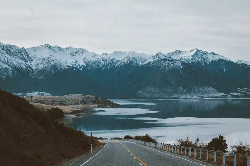 An open road wining around a mountain next to a lake, showing the route a mail carrier takes when shipping to Alaska.