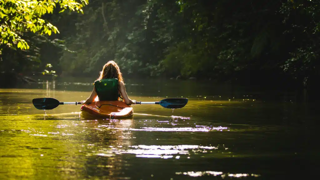 A woman is paddling away from the camera in a kayak on a river in Costa Rica, where Amazon does not deliver.