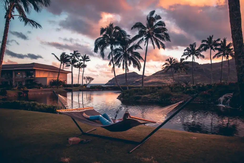Someone is laying in a hammock by their rental home in Hawaii, which they furnished using shipping companies to Hawaii. A sunset view is behind them.