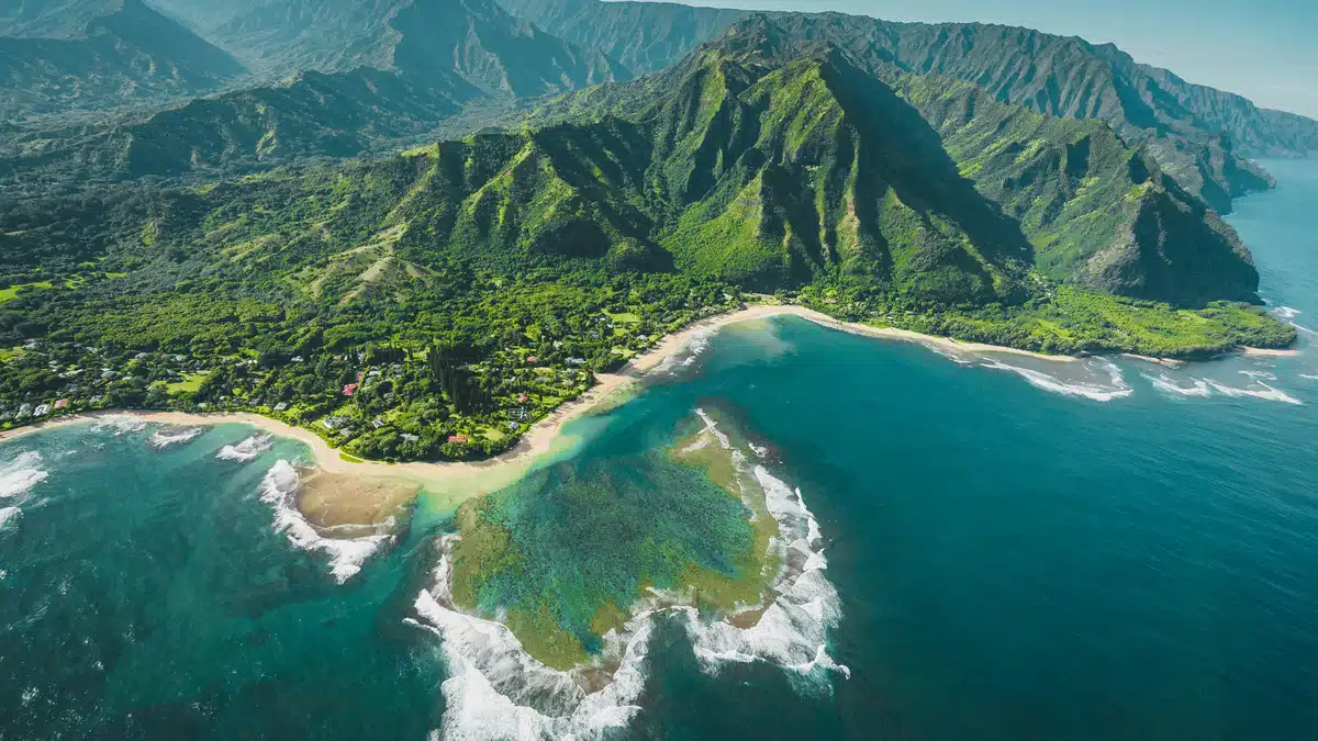 An aerial view of a Hawaiian coast, where white sand is meeting blue waters. Shipping to Hawaii often involves rocky waters like this.