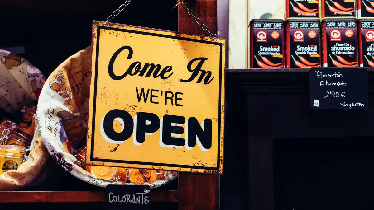 A sign that says 'Come in We're Open' is in the window of a small business.