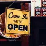 A sign that says 'Come in We're Open' is in the window of a small business.