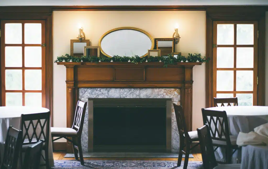 A large stone and wood mantle is over a fireplace in a dining room. The windows show a winter forest outside. Furniture stores that ship to Alaska furnish restaurants like this in remote locations.