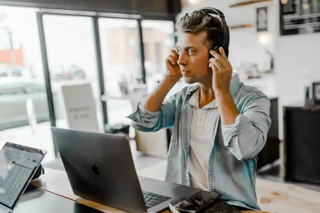 A guy is putting headphones over his ears as he gets ready to work on his laptop from a cafe. He is an owner of an ecommerce business looking for consolidated shipping services to help save him money.