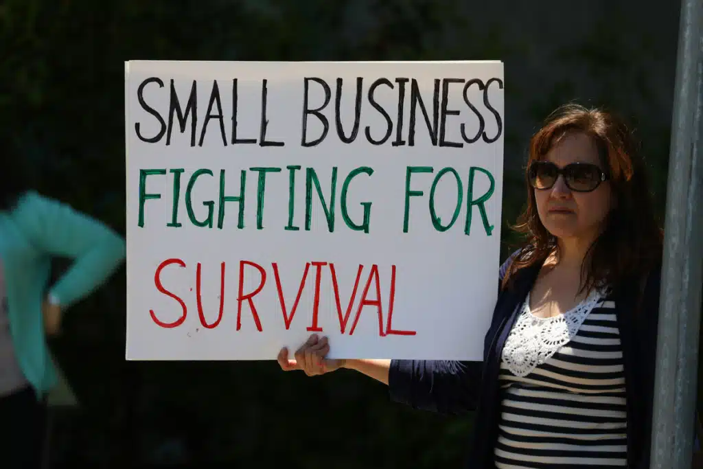 A woman is holding a sign that says 'small business fighting for survival'. Affordable shipping for small business means meeting the bottom line easier!