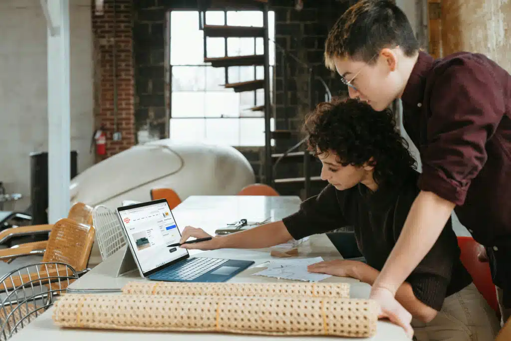 Two people are standing over a sewing table inside a small business. They're looking on a laptop to get the best shipping for small business.