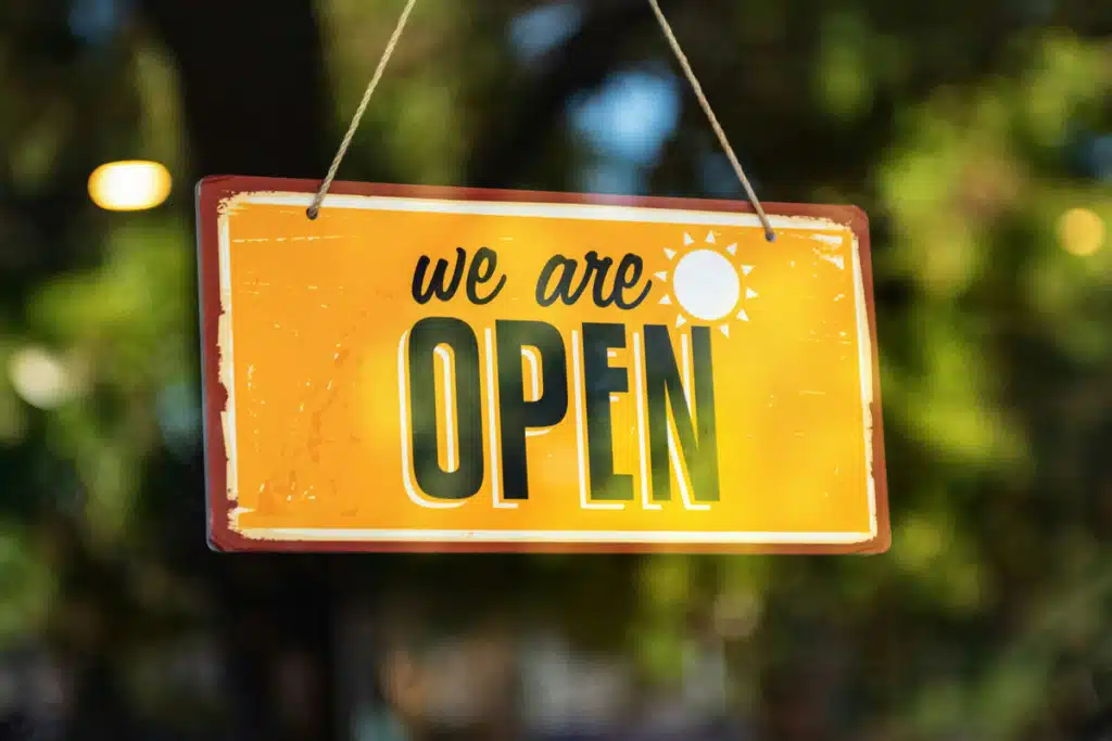 A yellow sign in a store window that says we are open.