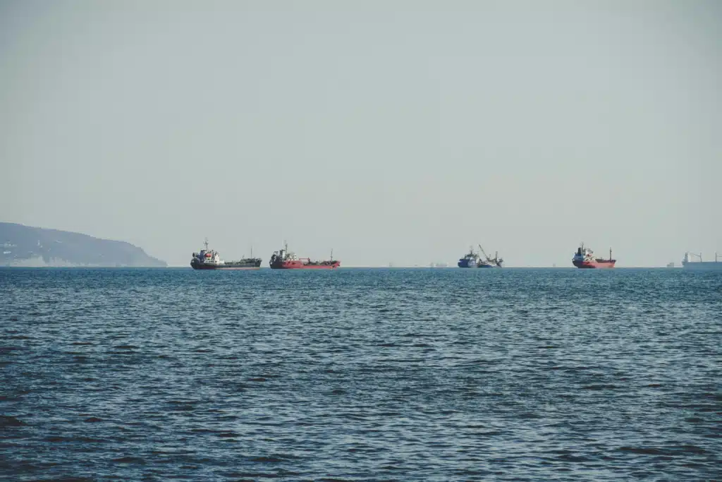 An open view of the sea with some land in the distance, and some cargo ships used for ecommerce international shipping.