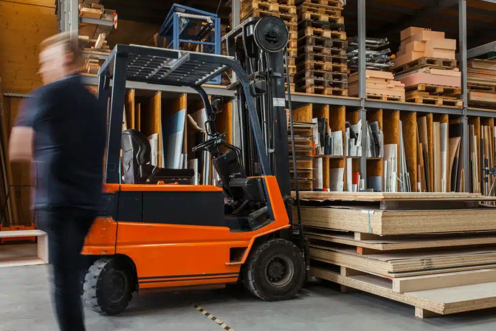 A man standing near a forklift in a warehouse, preparing to take inventory for order fulfillment.