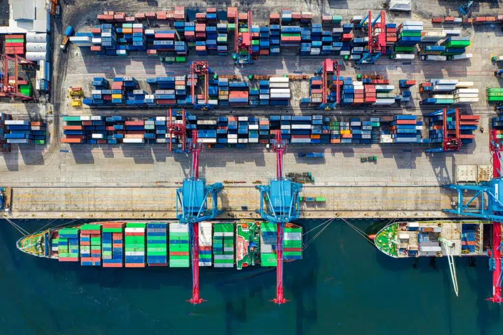 A cargo ship is being unloaded on a dock as it's shipping from US to China. It carries many varieties of goods.