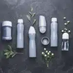 A selection of various sizes of aerosol cans against a dark grey background with leaves and flowers about. Can you ship aerosol cans like this? Find out here.