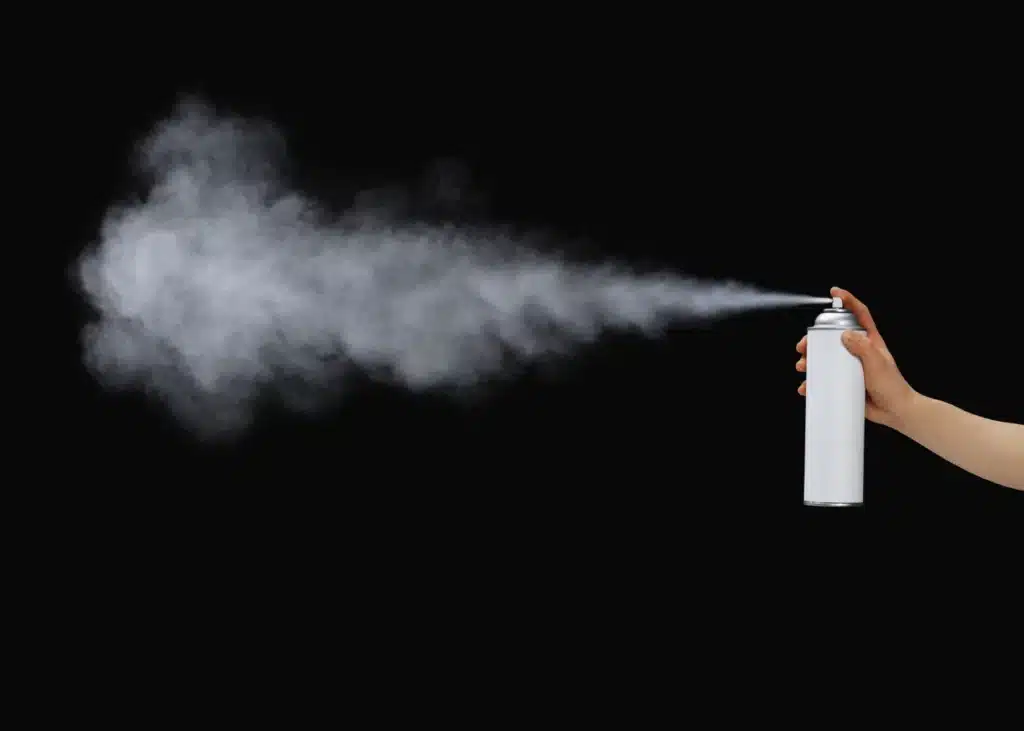 An aerosol can is spraying in front of a black background.