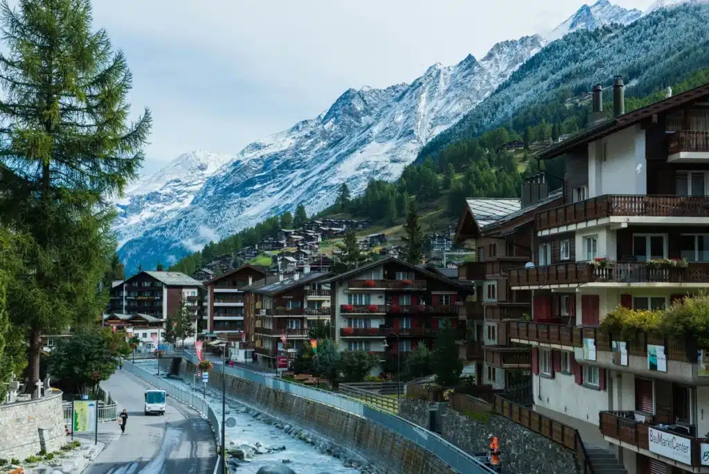 Apartments along a waterway, where shipping to Switzerland from US is easy with PostFromUS! Mountains are behind the buildings, almost towering over them. 