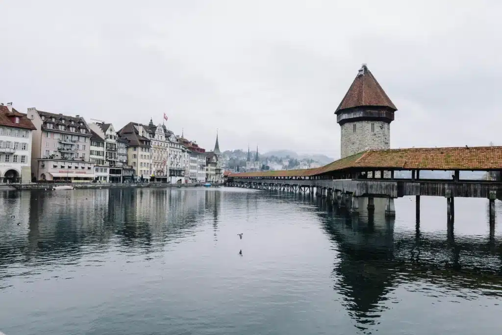 Une ville au bord de l'eau en Suisse, avec un long quai ou jetée sur la droite qui s'étend sur l'eau en direction de la ville.