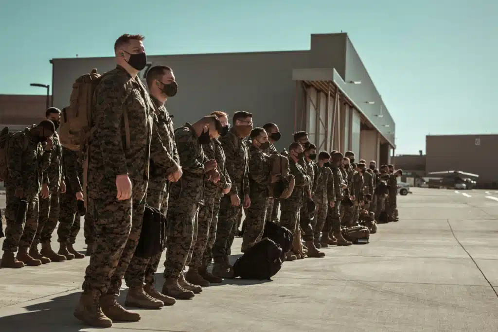 A group of US solders are lined up with luggage, wearing their uniforms and black PPE masks. Many of these soldiers will be expecting care packages to be sent to their military bases in the mail.