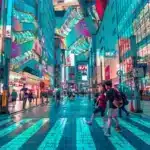 A busy city street is lit up during night time in Japan. Many people in these cities have access to American goods by shipping to Japan from US.