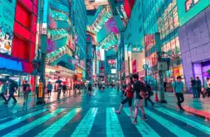 A busy city street is lit up during night time in Japan. Many people in these cities have access to American goods by shipping to Japan from US.