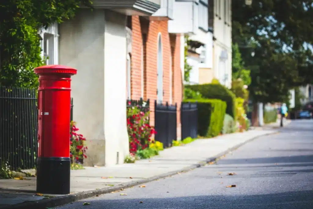 A residential street in England with a red post box on the left side of the sidewalk.