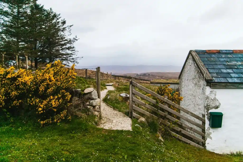 A remote cottage with a dirt path and wooden fence is ready to receive shipping to from the US to Ireland.