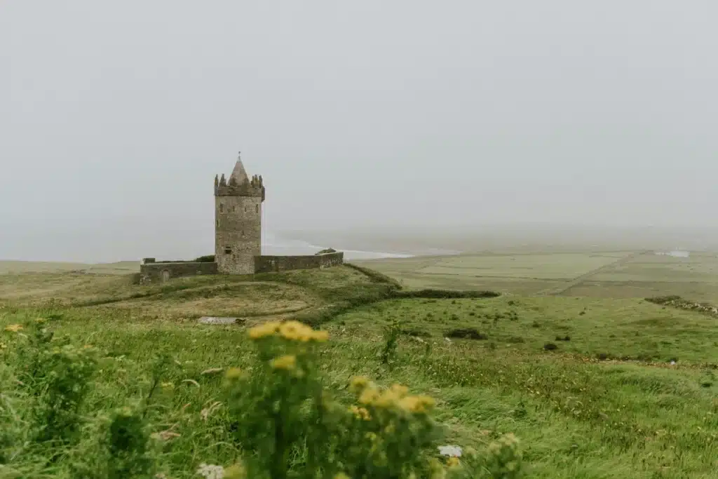 A castle in a foggy green field under a grey sky in Ireland.