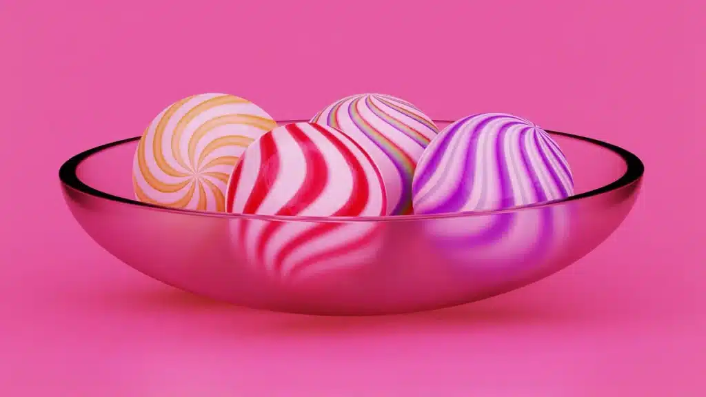 A low, wide, mid century candy dish that looks unique. It's filled with striped, swirly round candies. There is a hot pink background.